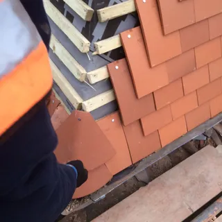 Roofer laying clay tiles at a lead valley during a re-roof in Lincoln